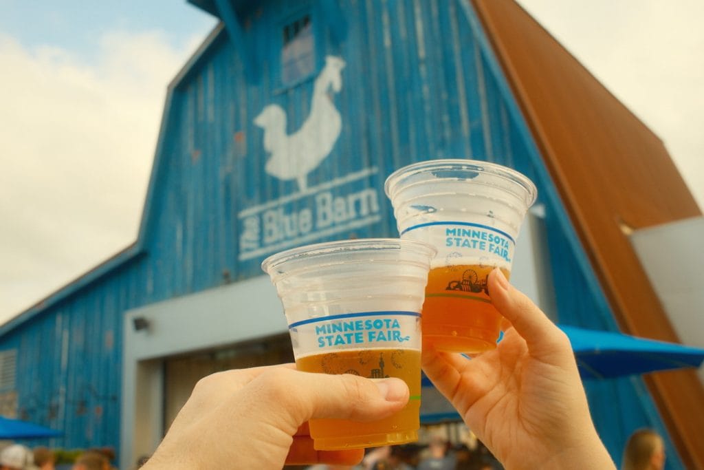 Two hands holding beers in front of the Blue Barn sign.