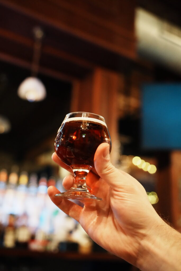 Hand holding a small glass of red beer up in the air.